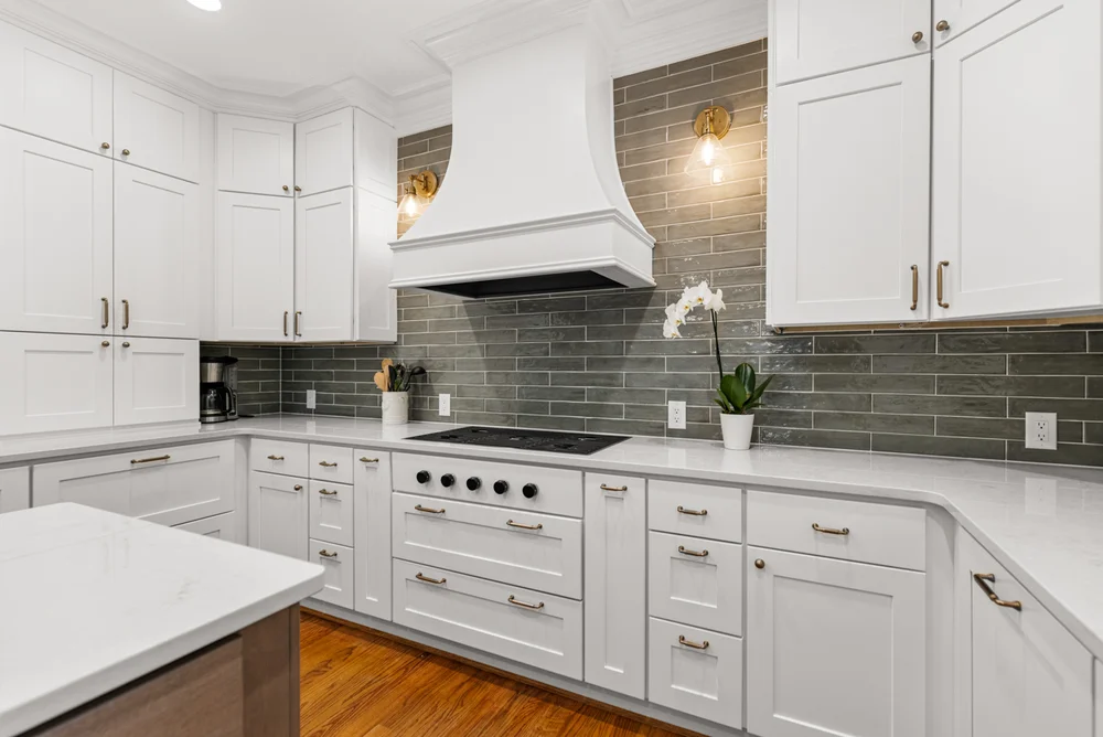 View of the range hood wall with custom hood, variated green tile, and a seamless range design
