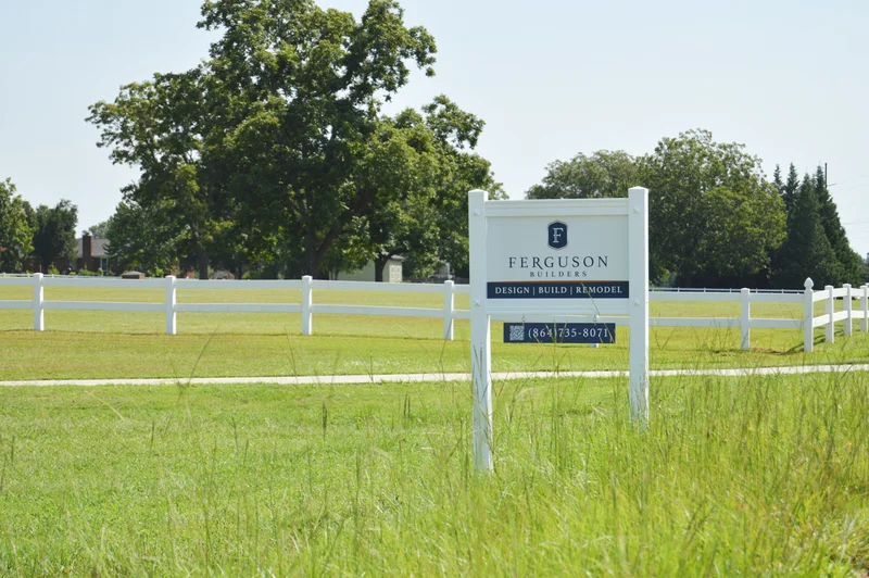 Ferguson Builders sign in an empty field with fence and trees in the background