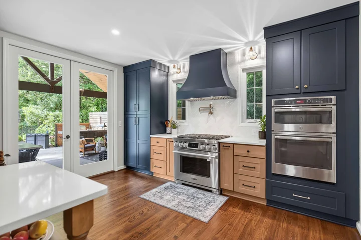 Kitchen remodel in upstate sc with wood and dark blue cabinetry, a large range hood and hardwood floors.