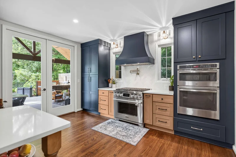 Kitchen remodel in upstate sc with wood and dark blue cabinetry, a large range hood and hardwood floors.