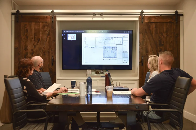 Conference room meeting with four people around a tv with plans on the screen